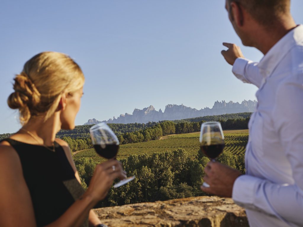 Parella fent un tast de vins amb vistes de vinyes i Montserrat de fons a les bodegues Oller del Mas / Marc Castellet